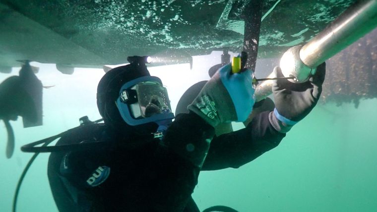 Diver in a full-face mask servicing a boat hull underwater